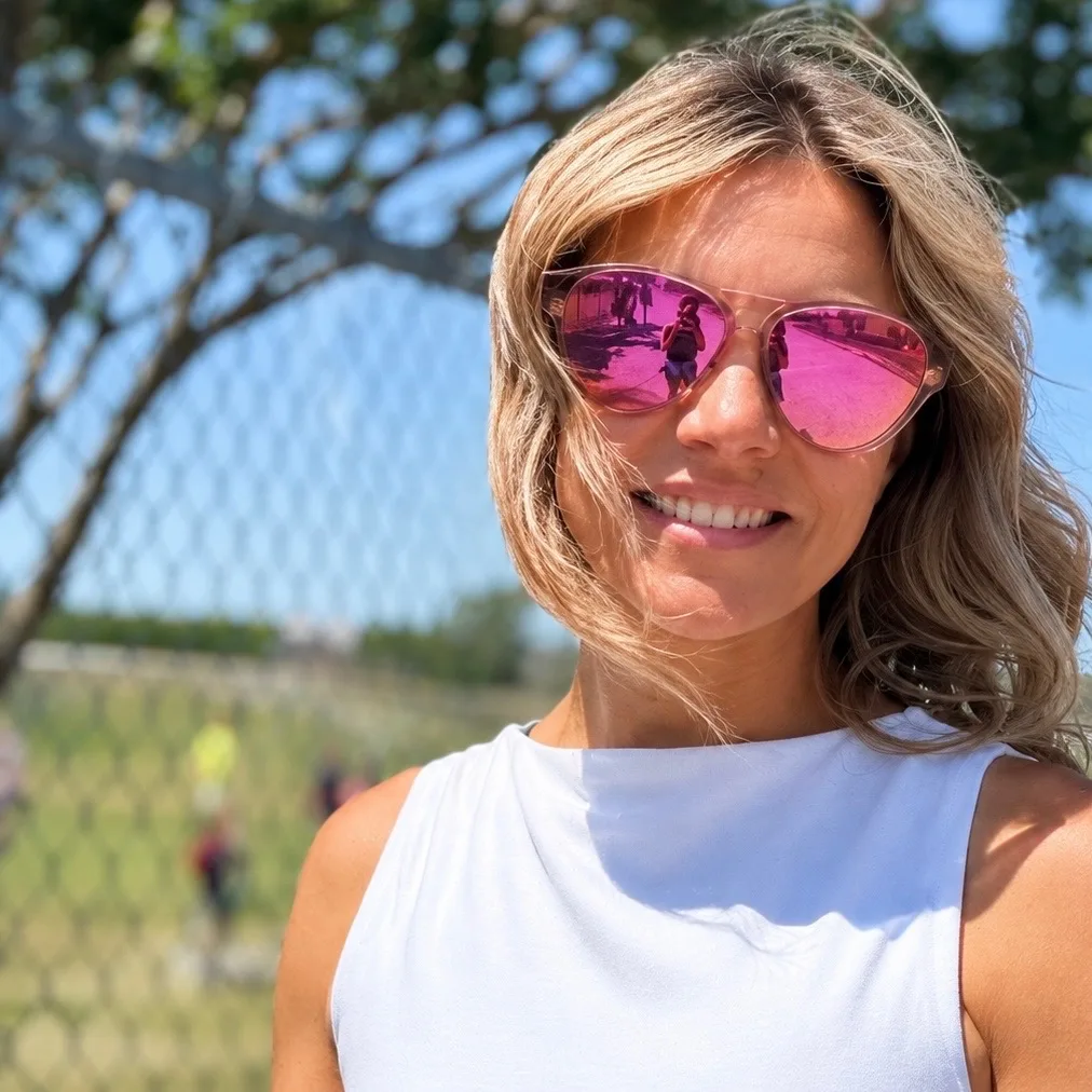 Angela, founder of Soccer Momster, smiling on the sideline in pink sunglasses